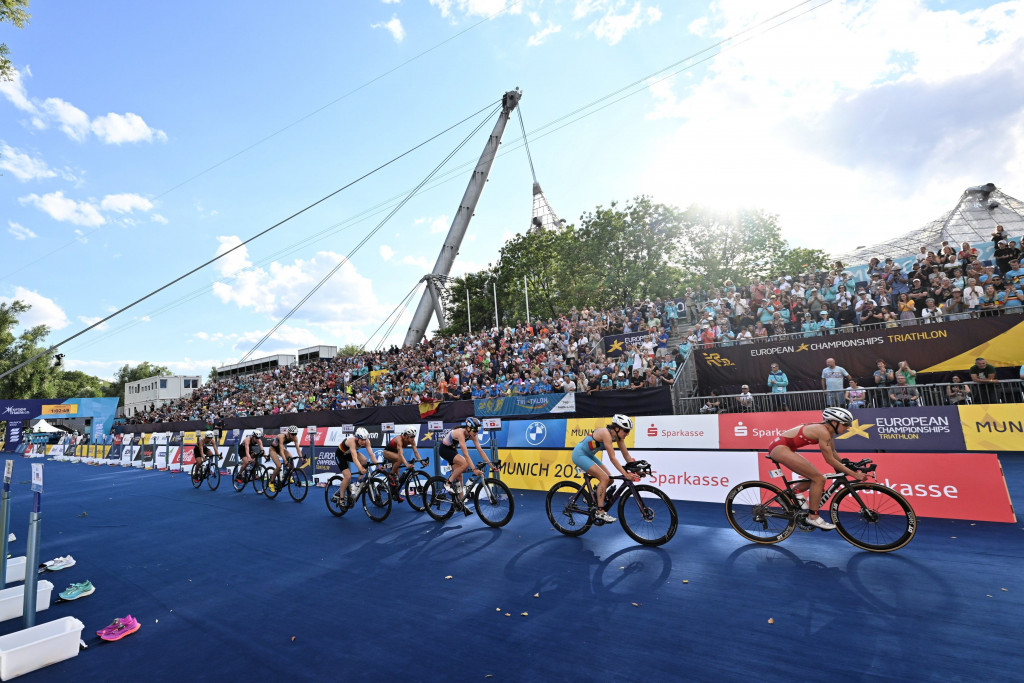 Gruppe Radfahrer fahren an Zuschauermenge vorbei, im Hintergrund das Olympiastadion